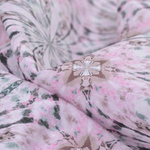 May include: Pink fabric with a white and grey abstract print. The fabric has a soft, flowing texture.