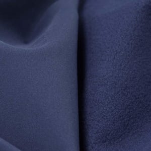 May include: Close-up of two navy blue fabrics. One is smooth and the other has a textured, fleecy appearance. The fabrics are folded, creating shadows and highlighting the different textures. This image showcases the contrast between the two materials.