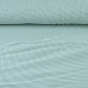 May include: A close-up of a light blue waffle knit fabric. The fabric is folded in half and has a soft, textured surface.