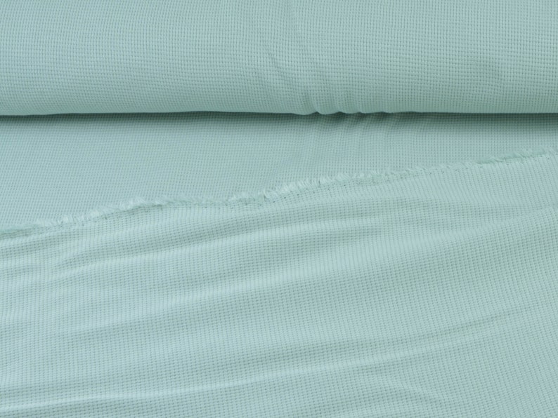 May include: A close-up of a light blue waffle knit fabric. The fabric is folded in half and has a soft, textured surface.