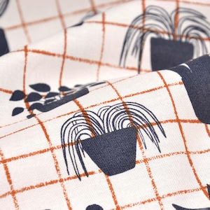 Puede incluir: Tela blanca con un patrón repetido de plantas en maceta sobre un fondo de cuadrícula. Las plantas son en blanco y negro y la cuadrícula es naranja.