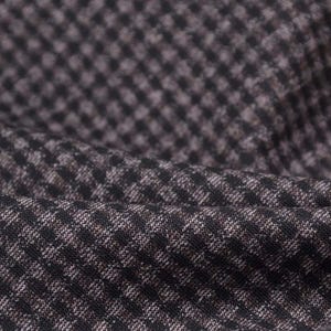 Könnte beinhalten: Nahaufnahme eines strukturierten Stoffes mit einem kleinen Karomuster. Der Stoff ist überwiegend dunkelgrau mit einem dezenten, helleren grauen Muster, das ein gewebtes Aussehen erzeugt. Der Stoff ist leicht drapiert und zeigt weiche Falten.