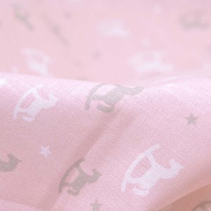 May include: Pink fabric with a repeating pattern of rocking horses and stars. The rocking horses are in shades of gray and white.