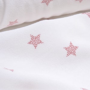 May include: White fabric with a repeating pattern of pink stars. The stars are made up of small pink dots.