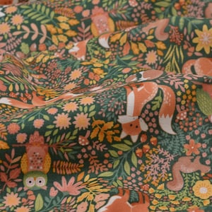 Könnte beinhalten: Ein Stoff mit Waldmotiv, der orange Füchse, Eulen und Eichhörnchen vor einem dunkelgrünen Hintergrund zeigt. Das Design umfasst orange, gelbe und rosa florale Elemente, die ein skurriles Waldmuster bilden.