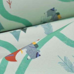 May include: Close-up of a fabric featuring a repeating pattern of bears, trees, and winding green roads. The bears are wearing hats and carrying backpacks. The fabric has a light green background with teal and red accents.