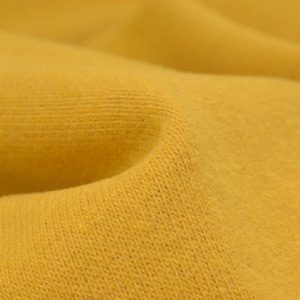 Könnte beinhalten: Nahaufnahme eines gelben Stoffes mit einer strukturierten Oberfläche. Der Stoff ist weich und hat einen dezenten Glanz.