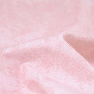 Pode incluir: Close-up de um tecido rosa claro e macio com um padrão sutil e texturizado. O tecido é drapeado, criando dobras e sombras suaves. O efeito geral é delicado e feminino, sugerindo um tecido para roupas ou decoração de casa.