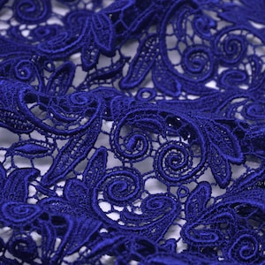 Könnte beinhalten: Nahaufnahme eines blauen Spitzenstoffes mit einem zarten Blumenmuster. Die Spitze ist filigran und hat eine weiche, fließende Textur.