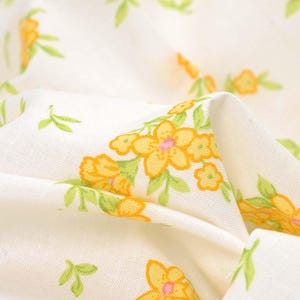 Puede incluir: Tela blanca con un patrón floral amarillo. La tela es suave y tiene un brillo sutil.