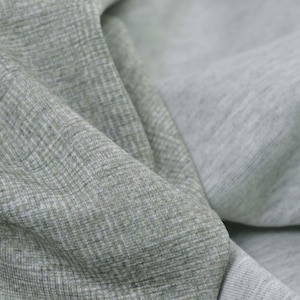 May include: Close-up of a grey fabric with a textured weave. The fabric is folded and draped, showing the different shades of grey.
