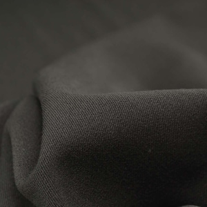May include: Close-up of a dark gray fabric with a textured weave. The fabric is folded and draped, showing its soft and smooth texture.
