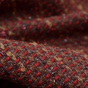 Könnte beinhalten: Nahaufnahme eines strukturierten Stoffes mit einem roten und braunen Tweed-Muster. Der Stoff hat einen dezenten Schimmer.