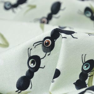 May include: A light green fabric with a repeating pattern of black ants. The ants have large, cartoon-like eyes.