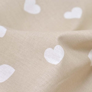 Puede incluir: Primer plano de una tela beige con un patrón repetido de corazones blancos. La tela está ligeramente arrugada, creando sombras y profundidad. Los corazones están espaciados uniformemente.