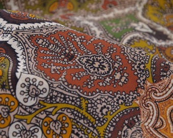 May include: Close-up of a fabric with a paisley pattern in shades of brown, green, and white.