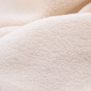 Puede incluir: Primer plano de una tela suave, blanquecina y texturizada. El material tiene un aspecto afelpado y esponjoso, con un pelo denso y rizado. La tela parece cálida y acogedora, posiblemente un material de forro polar o sherpa, ideal para ropa o decoración del hogar.