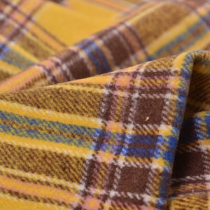 Op de afbeelding: Close-up van een gevouwen stof met een ruitpatroon. De stof heeft een combinatie van kleuren, waaronder geel, bruin, blauw, roze en wit. Het ruitontwerp is zichtbaar over het materiaal.