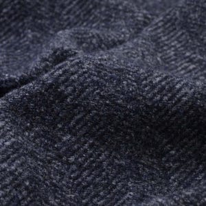 Può includere: Primo piano di un tessuto blu scuro con un motivo a spina di pesce. Il tessuto ha una consistenza morbida e testurizzata.