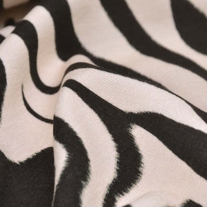 Peut inclure: Gros plan sur un tissu à imprimé zèbre blanc et noir. Le tissu a une texture douce et fluide.