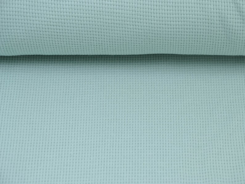 May include: A close-up of a light blue waffle knit fabric. The fabric has a textured surface and a soft, comfortable feel.