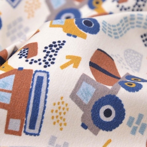 Könnte beinhalten: Nahaufnahme eines Stoffes mit einem sich wiederholenden Muster von Baumaschinen in Braun, Blau und Gelb auf cremefarbenem Hintergrund. Das Design umfasst Traktoren, Bagger und Pfeile, geeignet für Kinderkleidung oder Kinderzimmerdekoration.