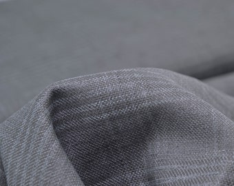 Könnte beinhalten: Nahaufnahme eines grauen, strukturierten Stoffes mit einem dezenten Fischgrätenmuster. Der Stoff ist weich und hat eine leicht zerknitterte Optik.