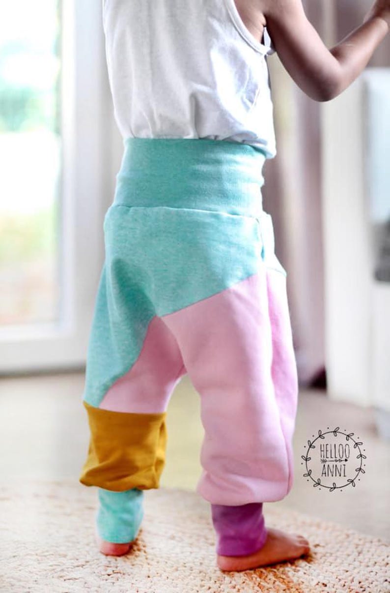 May include: Colorful toddler pants in shades of pink, teal, and mustard yellow. The pants have a high waistband and are made of soft fabric. The pants are designed with a unique color-block pattern.