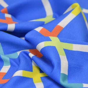 May include: Blue fabric with a geometric pattern of white, orange, yellow, and green lines. The fabric is folded and textured.