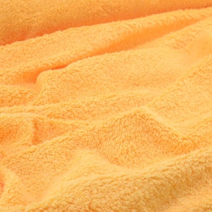 May include: A close-up of a soft, plush, orange fabric with a textured surface. The fabric is folded and wrinkled, creating a soft and inviting look.