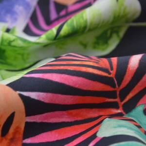 Peut inclure: Tissu noir avec un imprimé tropical composé de grandes feuilles vertes, de palmes roses et rouges et de fleurs orange et noires.