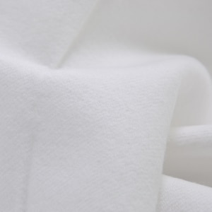 May include: Close-up of a white fabric with a textured surface. The fabric is folded and has a soft, smooth feel.