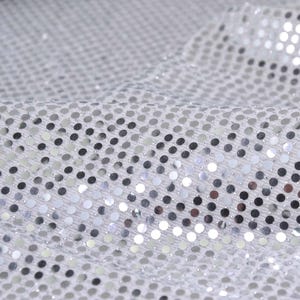 Peut inclure: Tissu de sequins argentés avec un léger éclat. Les sequins sont disposés en un motif répétitif.
