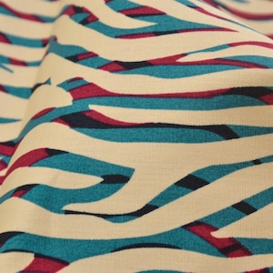 Pode incluir: Tecido de cor creme com um padrão de listras de zebra turquesa e bordô.