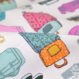 Pode incluir: Tecido branco com um padrão repetido de malas e câmeras coloridas. As malas são de vários estilos e cores, incluindo turquesa, rosa, laranja e verde. As câmeras são em preto e branco.