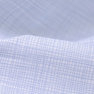 Pode incluir: Close-up de um tecido azul claro com um padrão de grade sutil. O tecido é liso e tem uma textura macia.