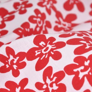 May include: White fabric with a red floral pattern. The flowers are stylized and have five petals.
