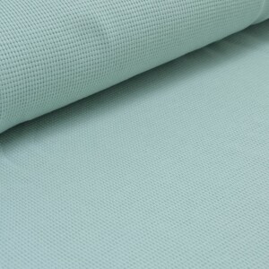 May include: A close-up of a light blue waffle knit fabric. The fabric has a textured surface and a soft, comfortable feel.