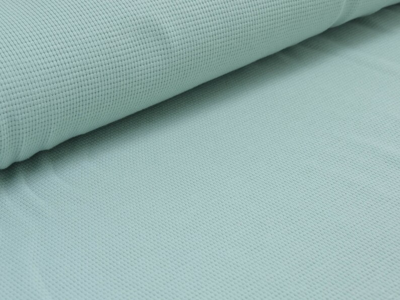 May include: A close-up of a light blue waffle knit fabric. The fabric has a textured surface and a soft, comfortable feel.