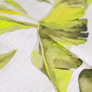 May include: Close-up of a white fabric with a green and yellow banana leaf print. The fabric has a soft, textured surface.