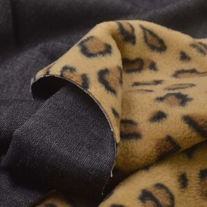 Könnte beinhalten: Nahaufnahme eines Stoffes mit Leopardenmuster in Beige- und Brauntönen. Der Stoff ist über einem dunkelgrauen Material geschichtet und zeigt eine denimartige Textur auf der Unterseite. Die Kanten zeigen den Kontrast zwischen den beiden Materialien.