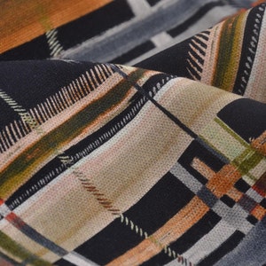 Op de afbeelding: Close-up van een stof met een ruitpatroon. Het ontwerp bevat een mix van kleuren, waaronder zwart, beige, oranje, groen en grijs. De stof is gevouwen en toont de textuur en de wisselwerking van de kleuren en lijnen.