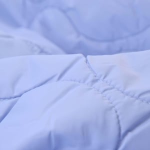 Peut inclure: Gros plan sur un tissu matelassé bleu clair. Le tissu présente un motif en losanges créé par les coutures. La matière semble douce et lisse, avec de subtiles variations de lumière. La texture suggère un article rembourré, comme une couverture.