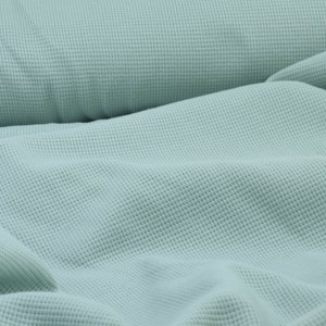 May include: A close-up of a light blue waffle knit fabric. The fabric is soft and textured, with a subtle sheen.