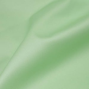 May include: A smooth, light green fabric with a subtle sheen. The fabric is folded in a way that creates soft, flowing lines.