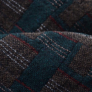 May include: Close-up of a fabric with a green, brown and red plaid pattern. The fabric has a textured, woven appearance.