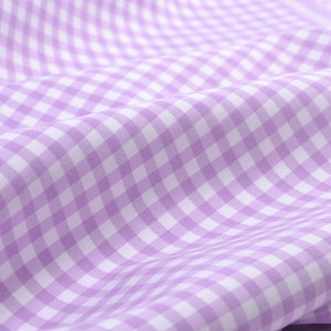 Könnte beinhalten: Nahaufnahme eines Stoffes mit Vichy-Muster in Lavendel- und Weißtönen. Der Stoff ist weich und hat sanfte Falten, wodurch ein strukturiertes Aussehen entsteht. Das Muster ist ein klassisches Design, geeignet für verschiedene Nähprojekte.