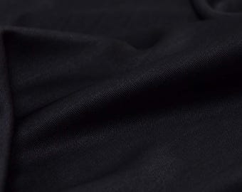 Peut inclure: Gros plan sur un tissu noir avec un tissage texturé. Le matériau est drapé, créant des plis et des ombres douces. La couleur sombre et la texture subtile suggèrent un textile de haute qualité, adapté à l'habillement ou à la décoration intérieure.