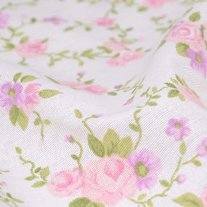 May include: White fabric with a pink and purple floral pattern. The fabric is soft and has a subtle texture.