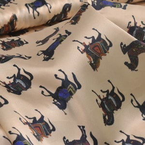Peut inclure: Tissu beige avec un motif répété de chevaux noirs avec des selles et des brides colorées.